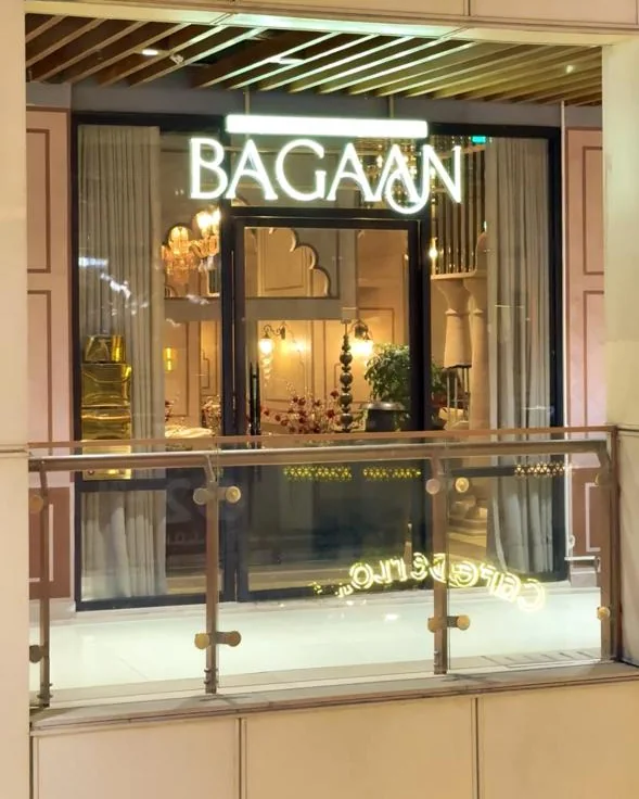 Bagaan's entrance at night — the illuminated BAGAAN sign above glass doors, with chandeliers and Mughal arches glowing inside.